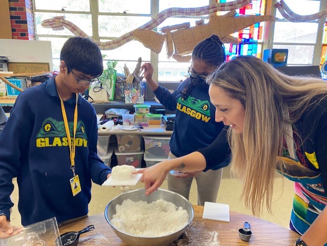 A teacher assisting two students with a sugar skull molding project