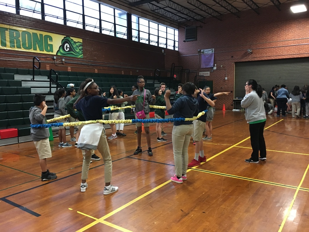 A group of students in the gym playing a game with a large, stretchy rope.