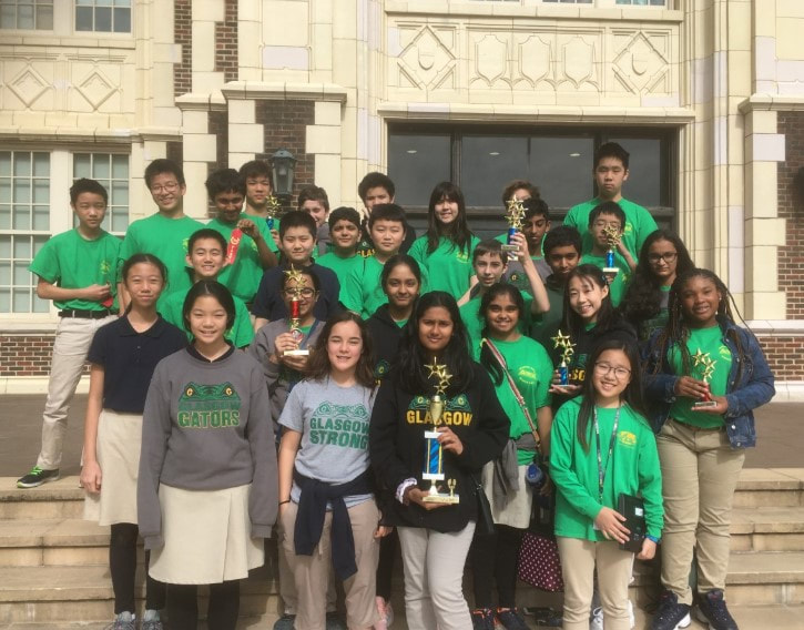 A large group of students posing for a photo in front of the school. Most are wearing matching shirts from the regional science fair. 