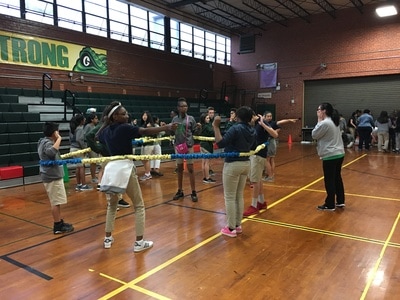 A group of students in the gym playing a game with a large, stretchy rope.