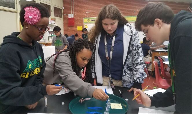 A group of students are gathered around a table. They are playing a science review game. 