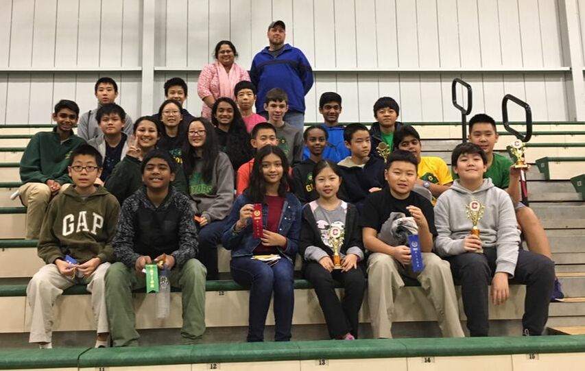 A large group of students and chaperones posing on the stairs at the Catholic High School math competition. Some students are holding trophies. 