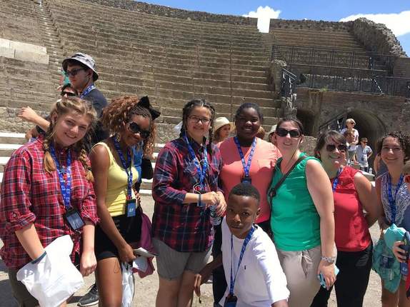 A group of students and adults in the Colosseum. They are smiling and happy. 